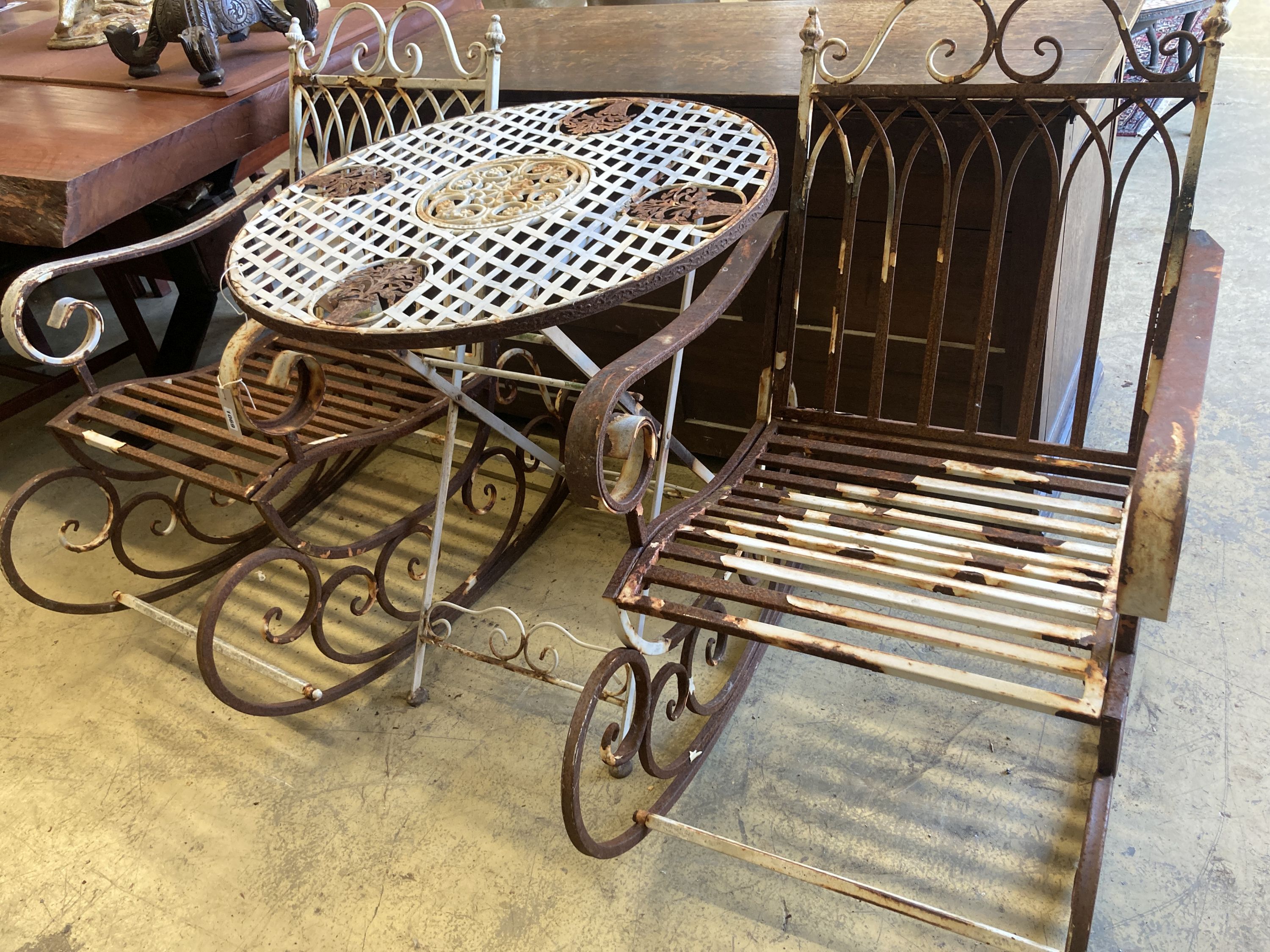 A pair of painted wrought iron garden rocking chairs together with a circular wrought iron folding garden table, diameter 71cm, height 76cm